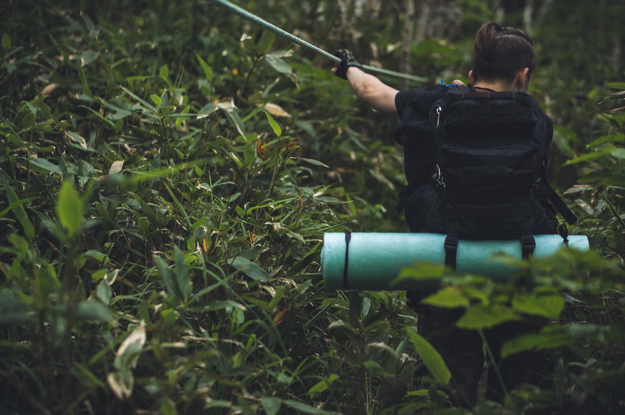 A person hiking through lush jungle with a backpack and rolled mat in tow.
